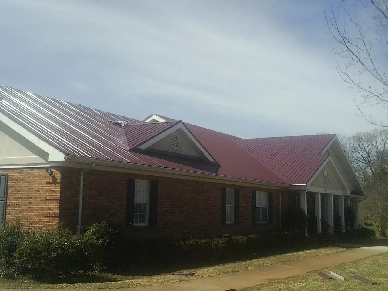Red metal roof with gabled entries on a long brick building, from a Hail Damage Roof Repair job in Beaufort