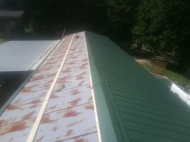 Old rusted panels beside newly installed green metal roofing — Wind Damage Roof Repair by Roofing Brothers in Beaufort